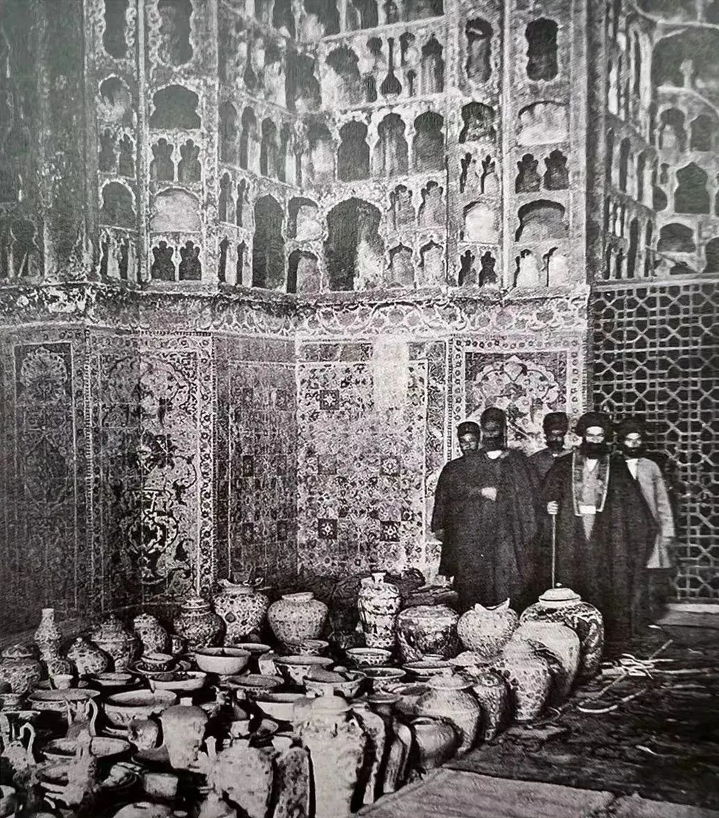 A photo of priests with servants and porcelain on the floor in the porcelain room of the Adbil Mosque Collection of the Boston Public Library